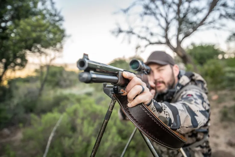 Hunter aiming a Henry rifle with a scope from a bipod mount on an African safari